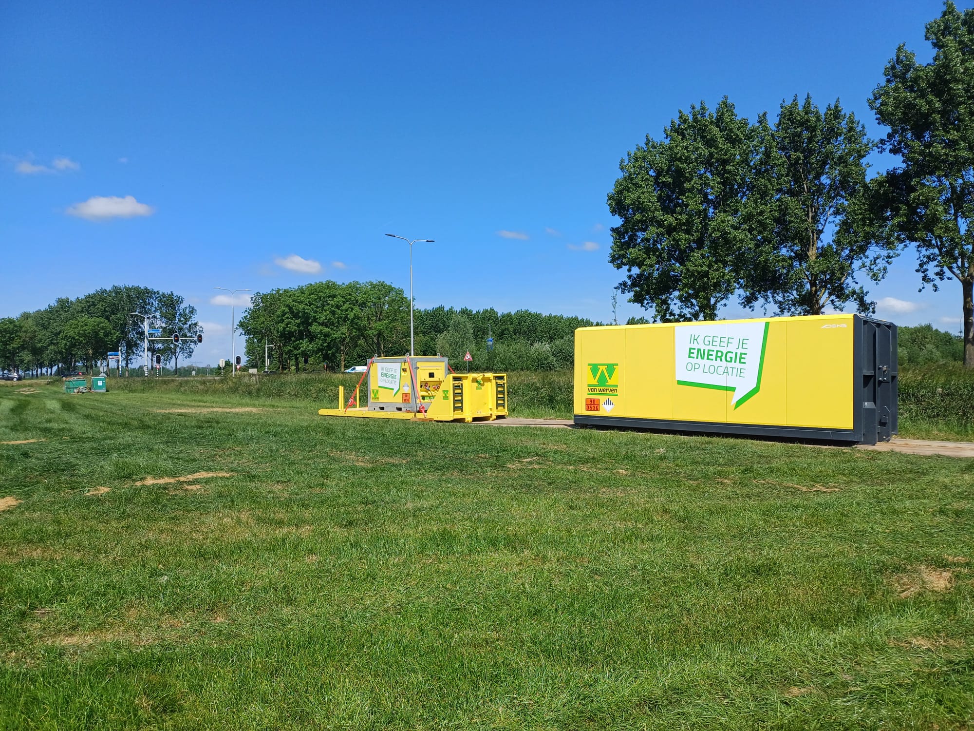Een gele Powerhub-container in de berm langs een weg, met verderop een kleiner geel batterijsysteem.
