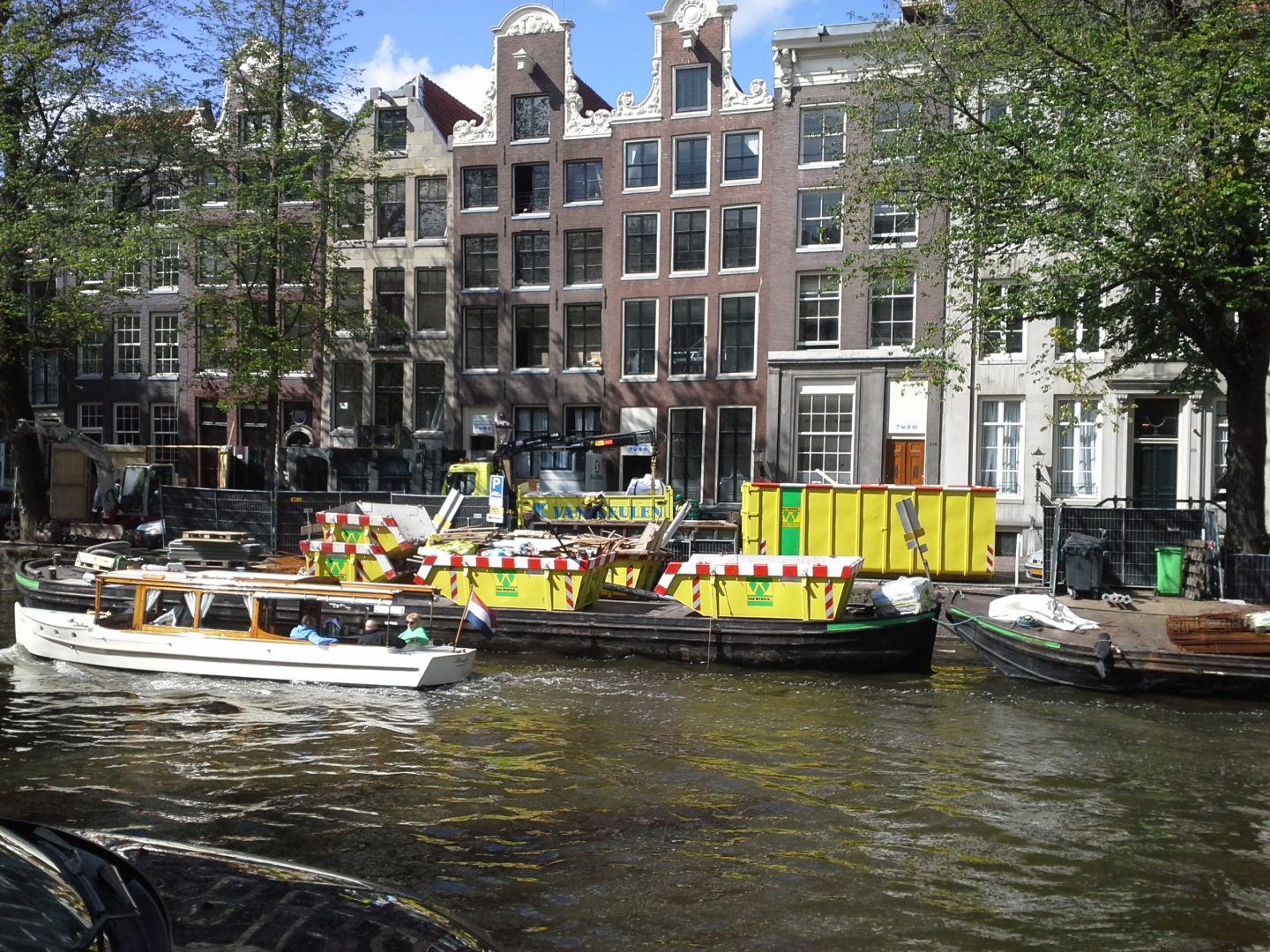Gele containers van Van Werven op een dekschuit in de Prinsengracht, voor de grachtenpanden van het Pulitzer Hotel, terwijl een rondvaartboot passeert